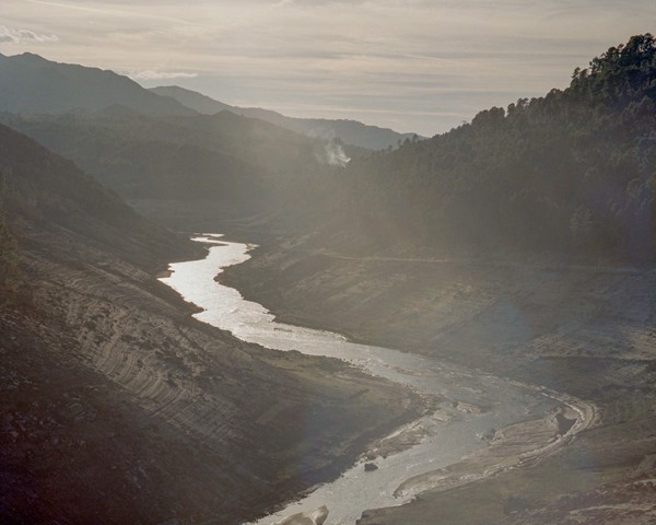 Vista del río Limia con niveles de agua muy por debajo de lo normal, visibles en las laderas montañosas expuestas. Este tramo
										pertenece al embalse de Lindoso, que en 2021 estuvo casi vacío tras la apertura de sus compuertas para aprovechar la
										subida del precio de la electricidad y maximizar los beneficios de la producción hidroeléctrica. Estas decisiones tienen un
										impacto sobre la biodiversidad, ya que las fluctuaciones del caudal alteran los ecosistemas fluviales, desplazan especies y
										afectan a su reproducción. Además, agravan el cambio climático al reducir la capacidad de los embalses para actuar como
										reservas de agua en periodos de sequía cada vez más frecuentes. La zona del río Limia también sufre contaminación debido
										al uso intensivo de fertilizantes y purines en la agricultura extensiva. Estas prácticas han degradado el agua y se asocian a
										un elevado porcentaje de casos de cáncer en la región, poniendo de relieve las consecuencias ambientales y de salud pública
										de este modelo agrícola expansivo.
