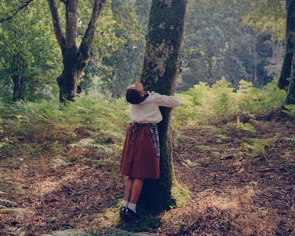 Sabela, una niña gallega, juega en los bosques de Palas de Rei abrazando un árbol, un gesto que encarna la profunda comunión
										del pueblo gallego con su entorno natural. Este bosque, lleno de vida e historias, contrasta de forma radical con los
										planes de la empresa portuguesa Altri, que pretende construir una planta de celulosa en las proximidades. Se prevé que la
										fábrica consuma 46 millones de litros de agua al día y promueva la expansión de monocultivos de eucalipto, una especie invasora
										que amenaza con sustituir la biodiversidad de estos bosques. El contraste entre la conexión simbólica de Sabela con
										la naturaleza y la agresividad de un modelo industrial como el de Altri refleja los dilemas ambientales y sociales a los que se
										enfrenta Galicia en la actualidad.