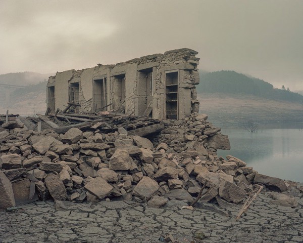 En enero de 1992, el embalse de Lindoso, gestionado por la empresa hidroeléctrica portuguesa EDP, sumergió los pueblos de
										Aceredo, Buscacalque, O Bao, Lantemil y A Reloeira, en la frontera entre Galicia y Portugal. Aquel día fatídico congeló estos
										pueblos en el tiempo, marcando el final de una era para sus habitantes. Tres décadas después, una grave sequía ha dejado el
										embalse de Lindoso casi vacío, sacando a la luz los restos de vidas que una vez prosperaron allí. En la imagen, los vestigios
										de una casa demolida en uno de estos pueblos sirven como un recordatorio inquietante del abandono que ha sufrido toda
										la región.