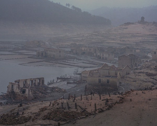 El pueblo de Aceredo, que emergió tras permanecer 30 años enterrado bajo las aguas del embalse de Lindoso, se erige como
										un recordatorio contundente de los efectos del cambio climático y del impacto destructivo de la acción humana sobre el
										entorno natural. Esta aldea, congelada en el tiempo bajo las aguas del embalse, evoca la abundancia de vida que una vez
										prosperó allí, donde las montañas y el río proporcionaban a sus habitantes todo lo necesario para su vida diaria. Tras el descenso
										del nivel del embalse, muchos antiguos vecinos, como Domingo Fontán, regresaron para contemplar lo que un día
										fue su hogar. Sin embargo, algunos, como Fontán, confiesan que hubieran preferido que el agua nunca se hubiese retirado,
										ya que volver a ver el pueblo de su infancia solo reabre heridas cuyo dolor resulta insoportable.