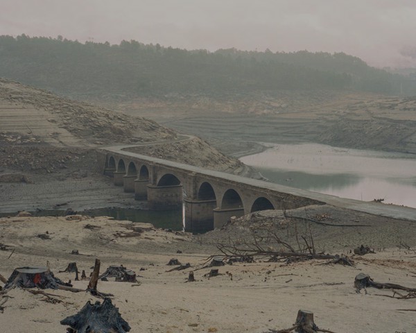 A Reloeira fue una pequeña aldea gallega sumergida bajo las aguas del embalse de Lindoso, también conocido como embalse
										de Aceredo, en Ourense. Este embalse, inaugurado en 1992 sobre el río Limia, formó parte de un proyecto hidroeléctrico
										entre España y Portugal. Su construcción supuso la expropiación y el desplazamiento de varias aldeas, entre ellas A Reloeira,
										Buscalque y O Bao, arrancando de raíz comunidades rurales que dependían de la agricultura, la ganadería y la pesca
										para subsistir.
										La pérdida de estas aldeas no fue solo física, sino también cultural y emocional, dejando un vacío en el tejido social de la
										región. La desaparición de A Reloeira plantea interrogantes sobre los sacrificios impuestos a las zonas rurales en nombre
										del desarrollo y refleja la historia de Galicia marcada por políticas de modernización que priorizan beneficios económicos
										a corto plazo frente a la preservación de su patrimonio humano y cultural.