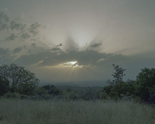 El sol se oculta tras una nube sobre el valle del Limia, visto desde Atás, el día del fallecimiento de mi abuela María. Para mí,
										este instante simbolizó una profunda conexión entre la vida y la muerte, donde lo místico y lo humano se entrelazan y el
										peso de las separaciones forzadas se hace evidente. María pasó gran parte de su vida como emigrante, dejando a su único
										hijo (mi padre) en Galicia. Años después, tras su regreso, su hijo falleció, víctima de un alcoholismo severo, un problema
										recurrente en la Galicia rural, impulsado por la soledad y la falta de oportunidades.