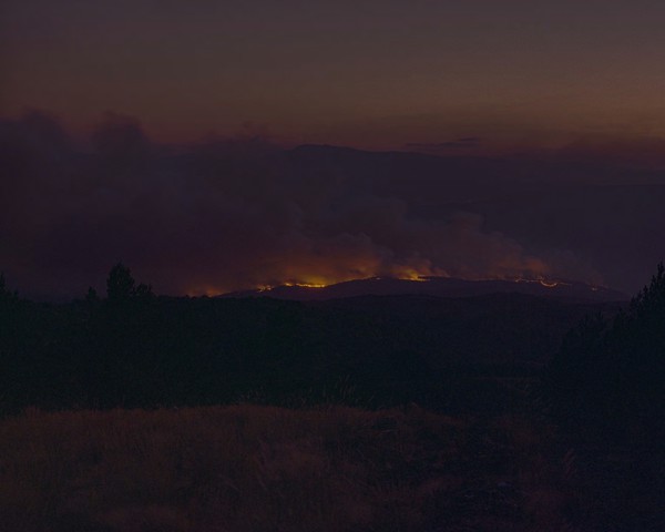 Durante la ola de incendios que arrasó mi pueblo y su entorno —Verín, Monterrei—, decidí subir al Alto do Foxo, para obtener
										una visión distante del fuego. Ante mí apareció una escena que me remitía de forma inevitable a las pinturas de Mark
										Rothko: dos o tres masas de color contenidas en una misma gama cromática. Esperé a que cayese un poco más la noche para
										que los tonos se oscurecieran y se igualaran, para que la imagen se volviese aún más abstracta. “No hay tal cosa como un
										simple registro del mundo”, escribió Susan Sontag. Toda imagen es una interpretación. Y es ahí donde esta fotografía empieza
										a incomodarme. No sé hasta qué punto es justo fotografiar un incendio de un modo que puede ser leído como bello.
										No sé si es legítimo convertir el desastre en una imagen contemplativa. Como se pregunta Sontag: ¿qué significa mirar el
										sufrimiento ajeno? ¿Dónde termina el testimonio y comienza la estetización? ¿Es justo convertir el dolor en icono, en forma,
										en color? Esta imagen no ofrece respuestas. Solo plantea dudas. Y quizá su sentido esté precisamente ahí: en ese espacio
										incómodo entre la distancia y la implicación, entre la belleza y el horror, entre mirar y cuestionar el propio acto de mirar.