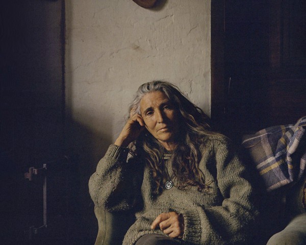 Guillermina, procedente de una familia de la ciudad de Lugo, decidió un día en su juventud romper con la vida urbana y
										marcharse a vivir a las montañas de Vilauxín, una aldea abandonada a la que solo se puede llegar caminando más de media
										hora tras otras dos horas de coche. Guillermina vivió su juventud en estas montañas dentro de una “comuna hippie”, criando
										a cuatro hijos, a los que dio a luz en su propia casa, sin médico ni instalaciones hospitalarias. Actualmente vive en Escanlar,
										una de las aldeas más remotas de la montaña gallega, donde la carretera termina y queda incomunicada durante épocas del
										año porque la nieve o las lluvias intensas destruyen los caminos. Dedica sus días a cortar leña, preparar la huerta y caminar
										por el bosque. Dos de sus hijos se han trasladado a la ciudad, mientras que otros dos viven en aldeas cercanas.