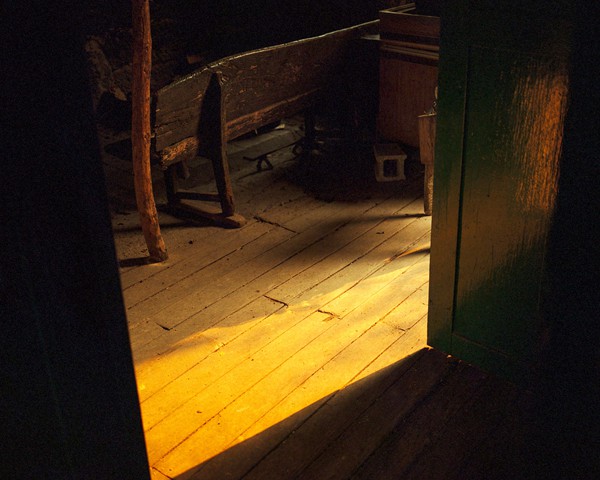 El interior de una casa abandonada desde hace 70 años en una aldea rural gallega se ilumina con una luz rojiza, filtrada por
										el humo de un incendio forestal. Galicia se encuentra entre las regiones más afectadas por la despoblación rural en España:
										más de 3.000 aldeas han sido abandonadas desde 1950, lo que ha dado lugar a montes sin gestionar y a una vegetación descontrolada
										que incrementa significativamente el riesgo de incendios. Esta falta de gestión del territorio es un factor clave
										en la elevada incidencia de incendios forestales en la región, donde en 2022 ardieron más de 24.000 hectáreas, superando la
										media de la última década. Casas abandonadas como esta reflejan el ciclo de despoblación y sus consecuencias ambientales.